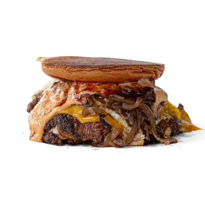 A messy burger with a toasted bun, melted cheese, grilled onions, and special sauce.