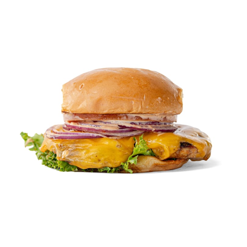 A chicken burger with melted cheese, red onion, lettuce, and sauce on a bun.